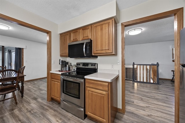 kitchen with stainless steel appliances, a textured ceiling, and light wood-type flooring