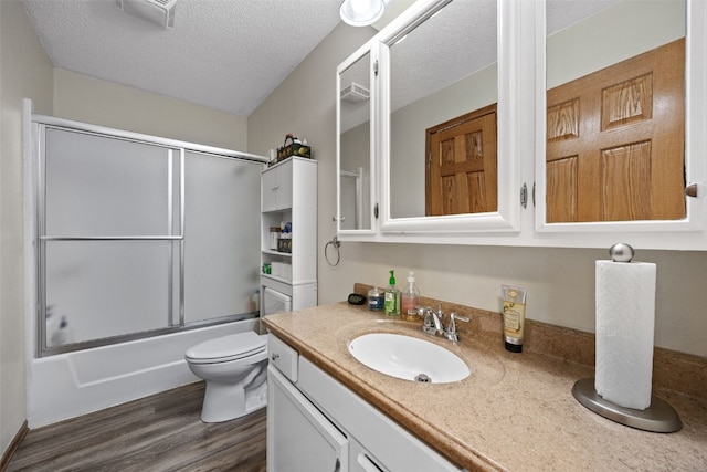 full bathroom featuring bath / shower combo with glass door, wood-type flooring, vanity, toilet, and a textured ceiling