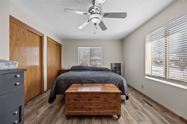 bedroom with ceiling fan, two closets, wood-type flooring, and a textured ceiling