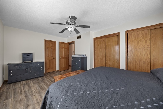 bedroom with dark hardwood / wood-style flooring, ceiling fan, a textured ceiling, and multiple closets