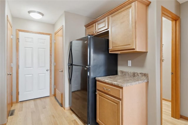 kitchen with light wood-type flooring, light brown cabinets, and black fridge