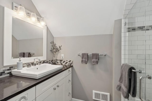 bathroom with tasteful backsplash, vanity, lofted ceiling, and a tile shower