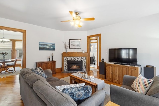 living room with ceiling fan with notable chandelier, light hardwood / wood-style floors, and a tile fireplace