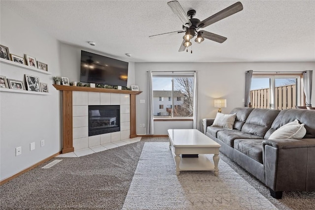 carpeted living room featuring ceiling fan, a tile fireplace, and a textured ceiling