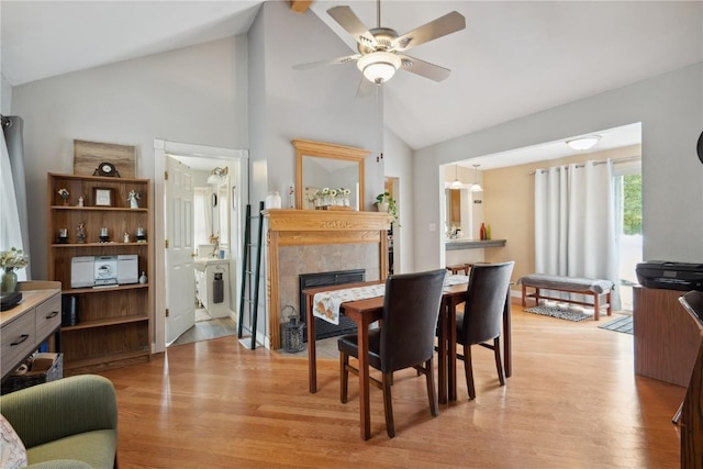 dining room with ceiling fan, high vaulted ceiling, a fireplace, and light hardwood / wood-style flooring