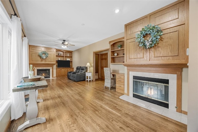 living room featuring a fireplace, built in features, ceiling fan, and light hardwood / wood-style flooring