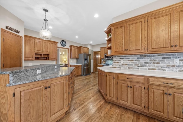 kitchen featuring decorative light fixtures, light stone countertops, stainless steel fridge, light hardwood / wood-style floors, and decorative backsplash