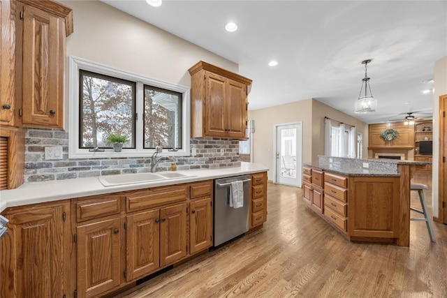 kitchen with light hardwood / wood-style flooring, sink, decorative light fixtures, stainless steel dishwasher, and a breakfast bar area