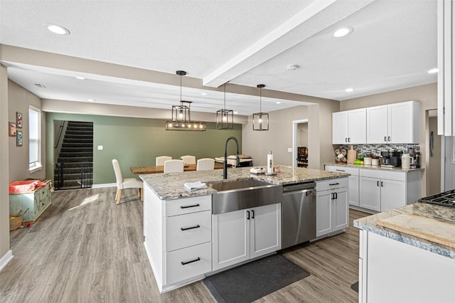 kitchen with pendant lighting, dishwasher, white cabinetry, light hardwood / wood-style floors, and a center island with sink