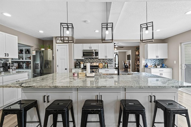 kitchen featuring white cabinetry, hanging light fixtures, a large island with sink, and appliances with stainless steel finishes