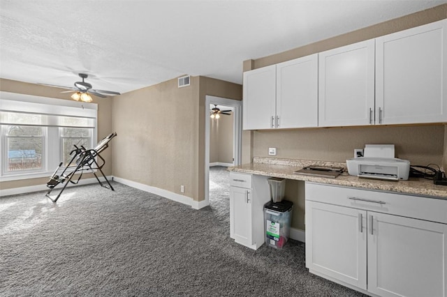 kitchen with white cabinetry, dark carpet, light stone countertops, and ceiling fan