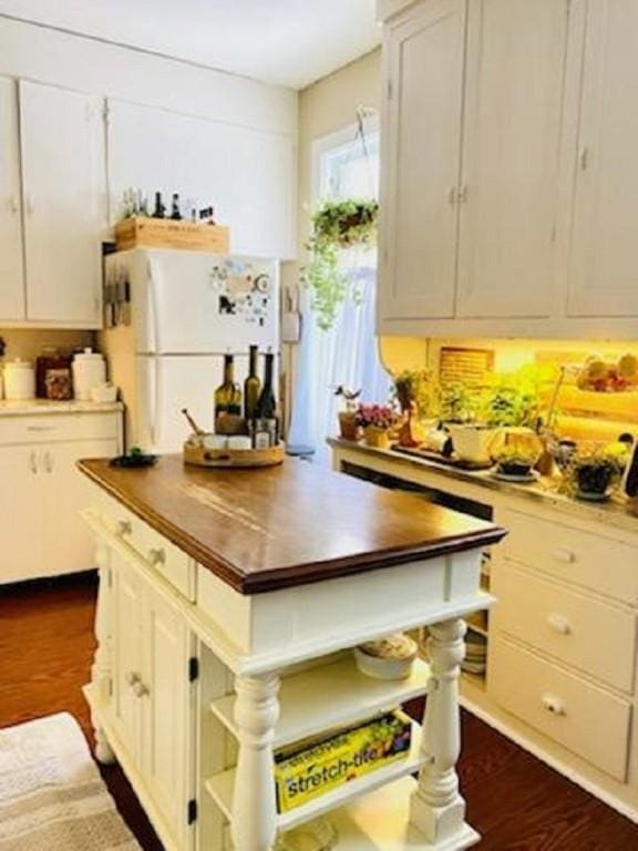 kitchen featuring dark hardwood / wood-style flooring, wood counters, white cabinets, and white fridge