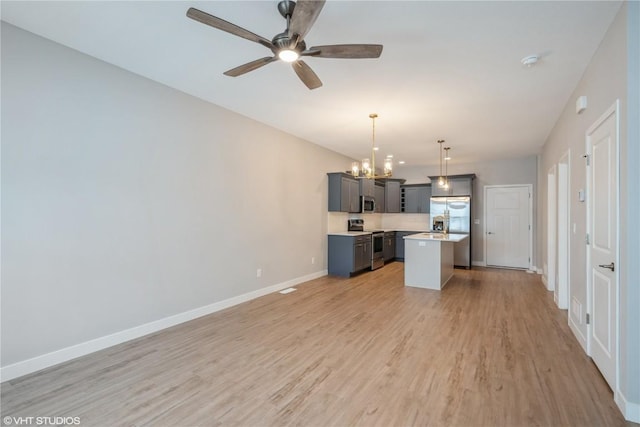 kitchen with appliances with stainless steel finishes, gray cabinets, a center island, light wood-type flooring, and hanging light fixtures