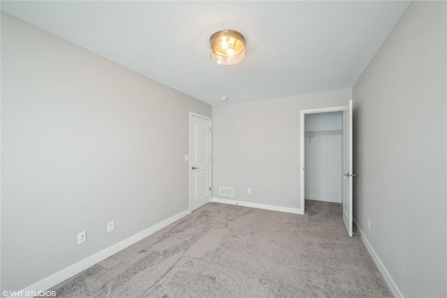 unfurnished bedroom with light carpet and a walk in closet