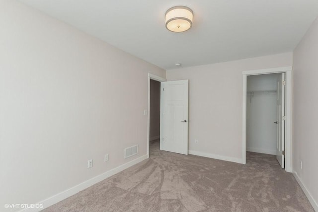 unfurnished bedroom featuring carpet, a walk in closet, and a closet