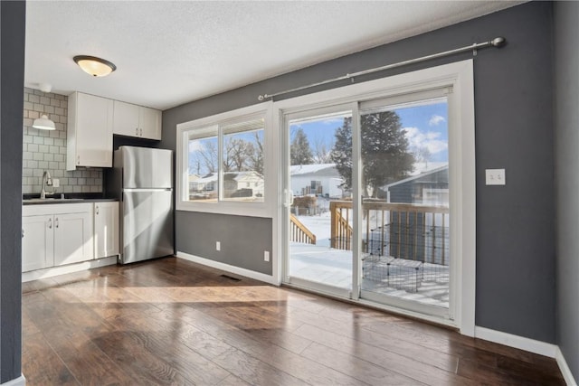 kitchen with white cabinets, stainless steel refrigerator, backsplash, dark hardwood / wood-style flooring, and sink