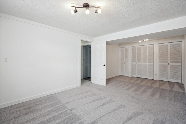 unfurnished bedroom with light colored carpet, multiple closets, and a textured ceiling