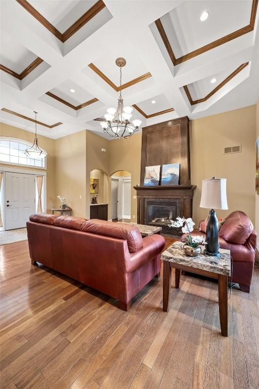 living room featuring hardwood / wood-style flooring, a notable chandelier, a large fireplace, coffered ceiling, and crown molding