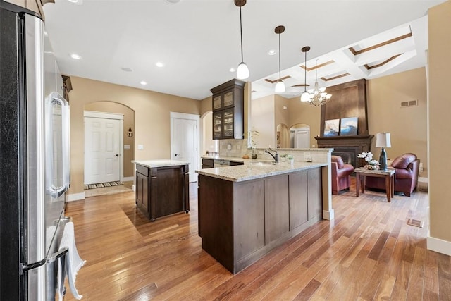 kitchen featuring kitchen peninsula, hanging light fixtures, stainless steel fridge, and dark brown cabinetry