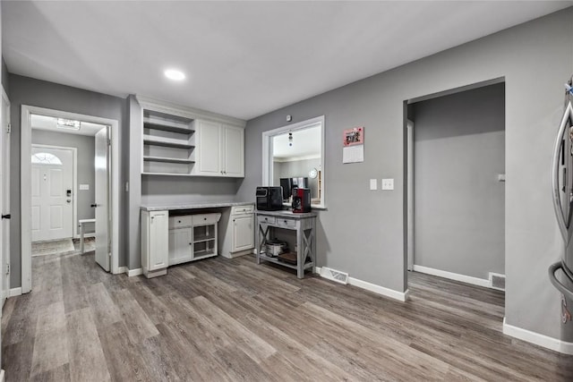 kitchen with white cabinetry, built in desk, and wood-type flooring