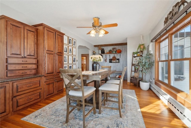 dining area with light wood-style floors, a baseboard radiator, ceiling fan, and arched walkways