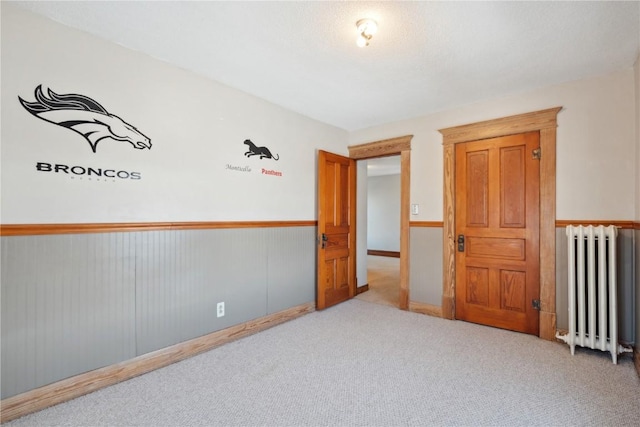 spare room with a wainscoted wall, carpet floors, and radiator