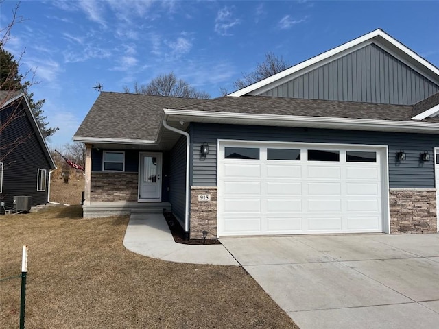 view of front of property with a garage, stone siding, central air condition unit, and roof with shingles