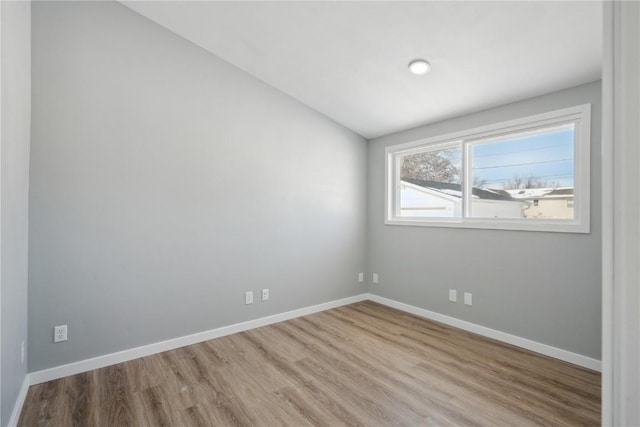 empty room with lofted ceiling, light wood finished floors, and baseboards