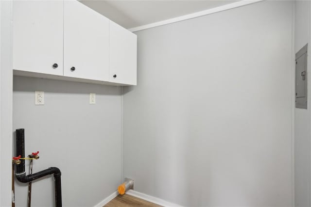 clothes washing area featuring light wood finished floors, hookup for a washing machine, cabinet space, electric panel, and baseboards