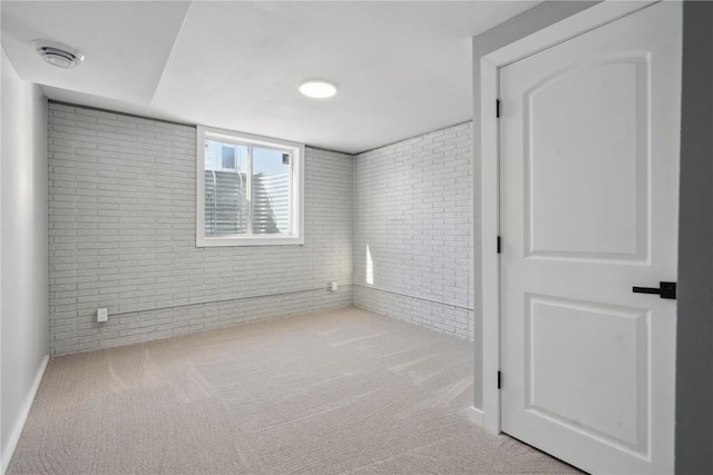 empty room with light colored carpet, visible vents, and brick wall