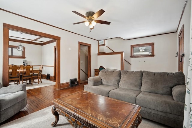 living area featuring baseboards, ceiling fan, wood finished floors, stairs, and crown molding