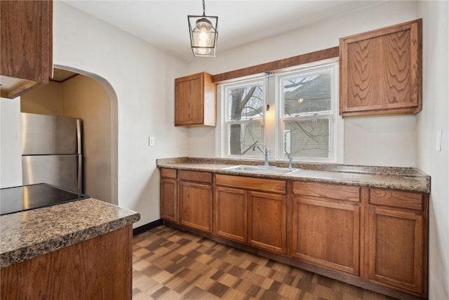 kitchen with arched walkways, decorative light fixtures, dark countertops, freestanding refrigerator, and a sink