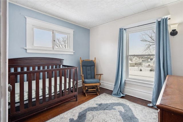 bedroom featuring a crib, baseboards, dark wood-type flooring, and ornamental molding