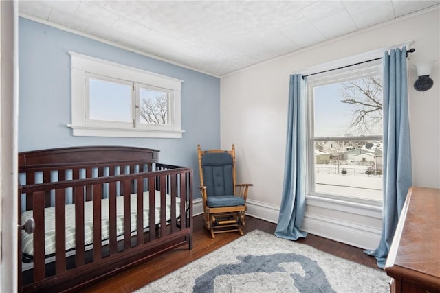 bedroom featuring crown molding, dark wood-type flooring, a crib, and baseboards