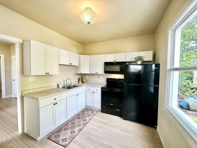 kitchen featuring white cabinets, light wood-style flooring, light countertops, black appliances, and a sink