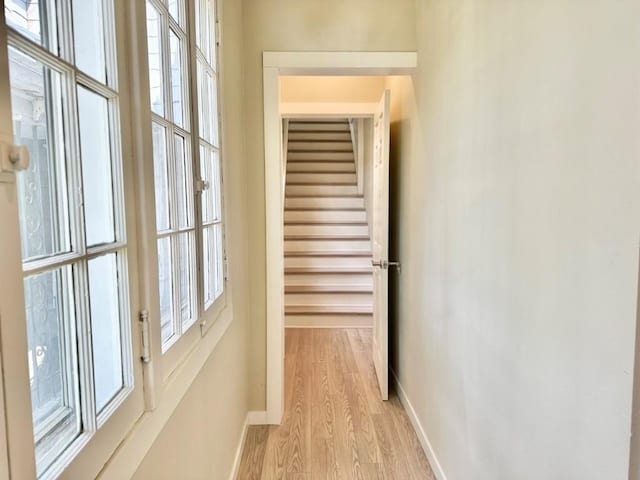 hallway featuring light wood-style floors, baseboards, and a wealth of natural light