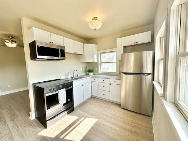 kitchen with light wood-style flooring, appliances with stainless steel finishes, white cabinets, and a sink