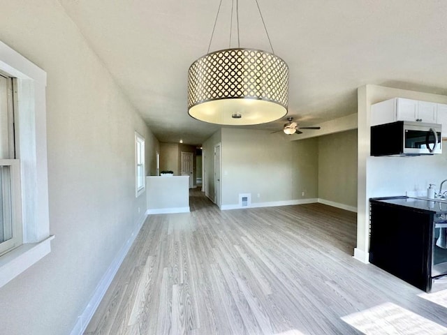 unfurnished living room with light wood-style floors, visible vents, baseboards, and a ceiling fan