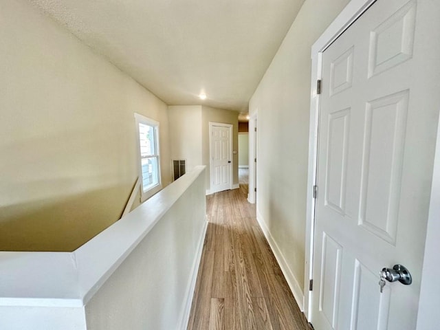 hall featuring baseboards, visible vents, wood finished floors, and an upstairs landing