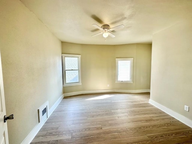 spare room featuring light wood-type flooring, visible vents, ceiling fan, and baseboards