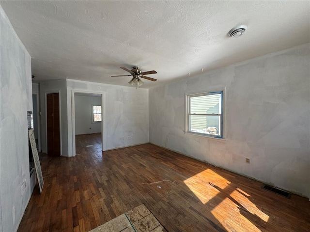 empty room with dark wood-style floors, a ceiling fan, visible vents, and a textured ceiling