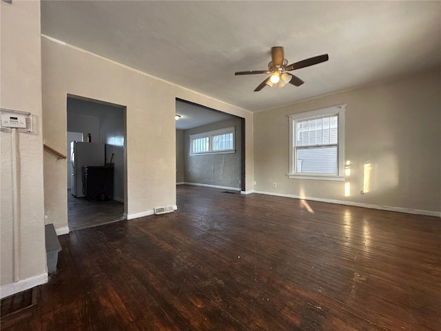 unfurnished living room featuring dark wood-style floors, ceiling fan, visible vents, and baseboards