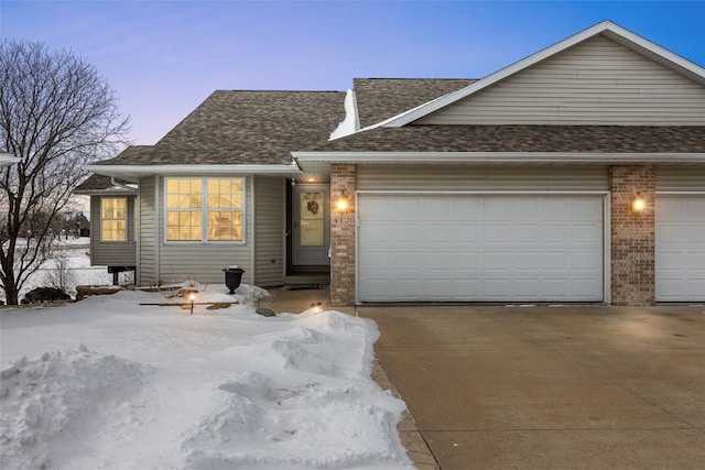 view of front of home featuring driveway, an attached garage, a shingled roof, and brick siding