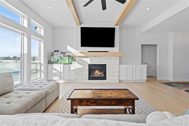 living room featuring light wood-style flooring, a fireplace, a ceiling fan, baseboards, and beamed ceiling