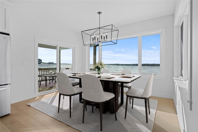 dining space with plenty of natural light, a water view, a chandelier, and light wood-style flooring