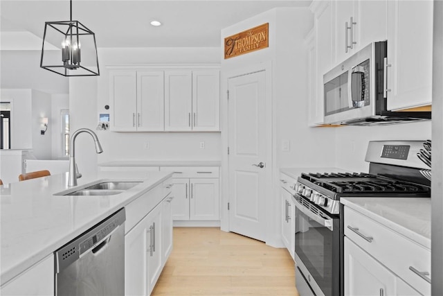 kitchen with appliances with stainless steel finishes, white cabinets, a sink, and decorative light fixtures