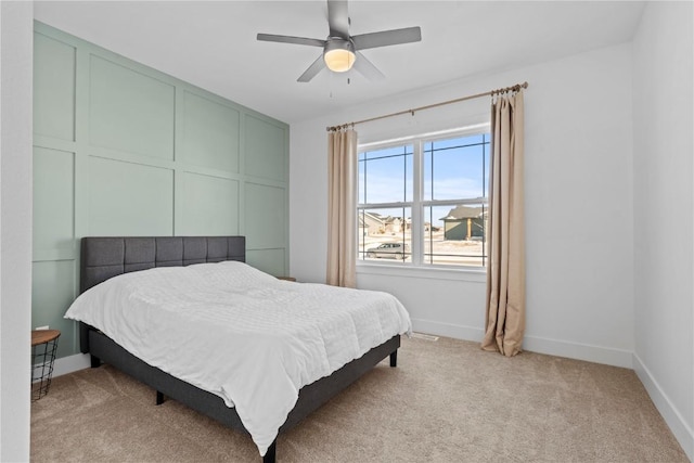 bedroom featuring light carpet, ceiling fan, baseboards, and a decorative wall