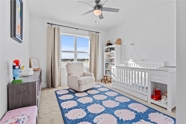 bedroom featuring a nursery area, ceiling fan, light carpet, and baseboards