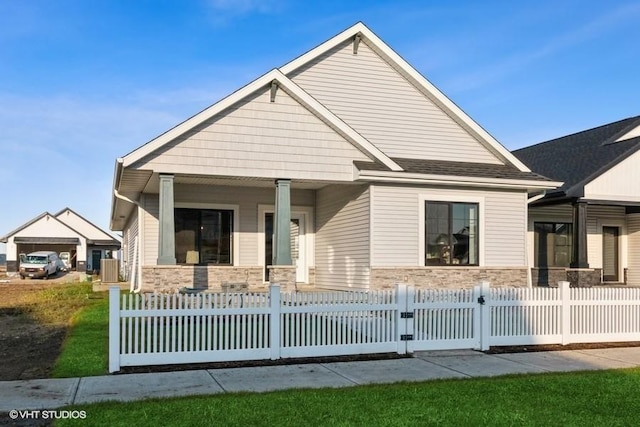 view of front of house with a fenced front yard, stone siding, and covered porch