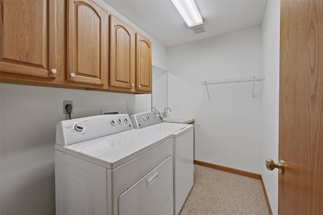 washroom featuring a textured ceiling, separate washer and dryer, a sink, baseboards, and cabinet space